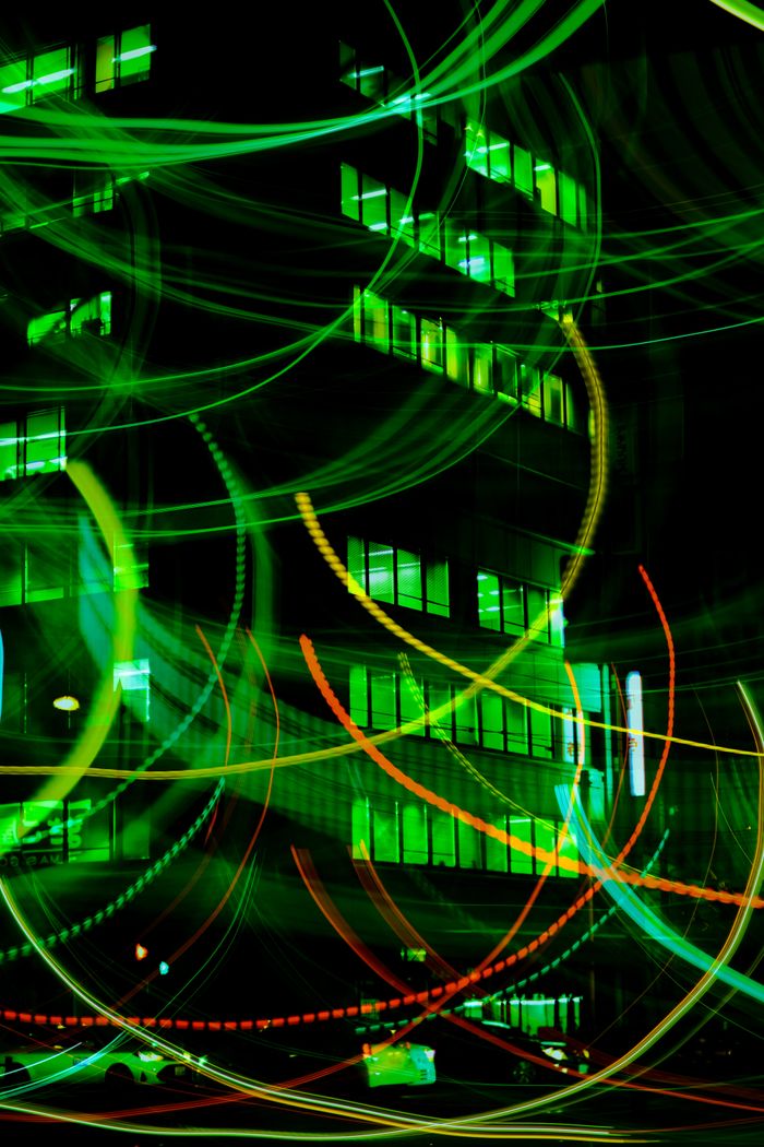 Vibrant light trails against a city building backdrop create a dynamic urban night scene.