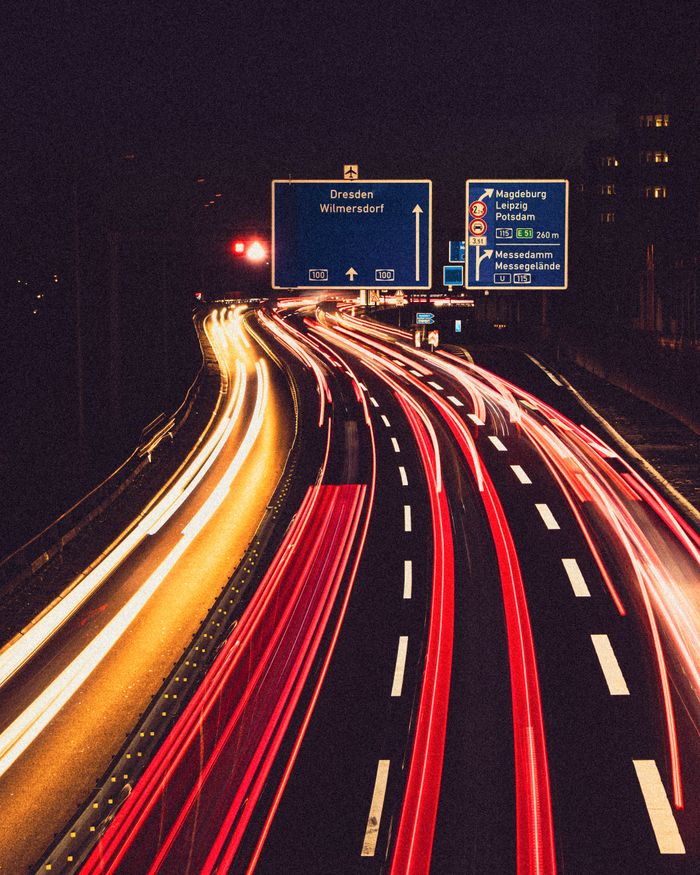 Long exposure of light trails on autobahn with Dresden signage, creating dynamic motion effect at night.